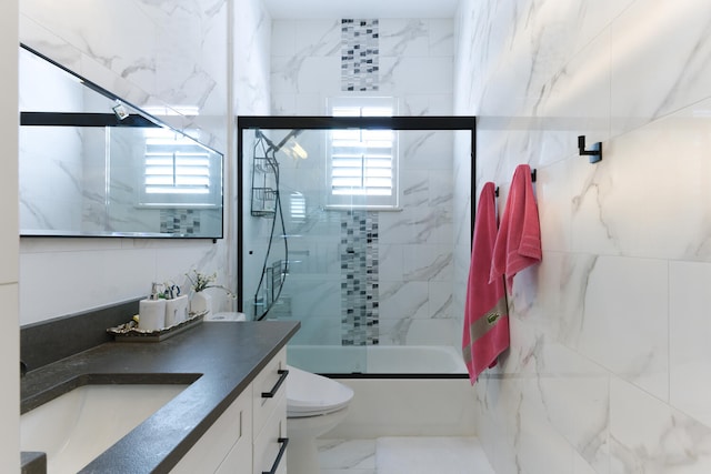 full bathroom with toilet, marble finish floor, combined bath / shower with glass door, tile walls, and vanity