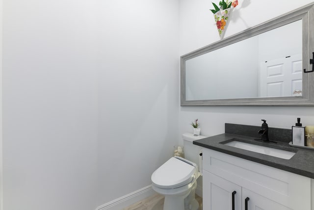 half bathroom featuring toilet, vanity, and baseboards