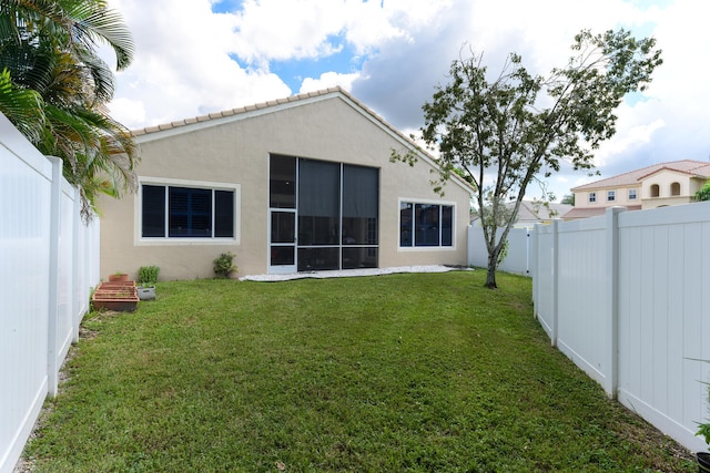 back of house with a yard, stucco siding, a fenced backyard, and a sunroom