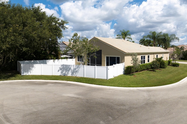 view of side of home featuring stucco siding, a tiled roof, a yard, and fence