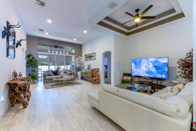 living room with wood finished floors, visible vents, arched walkways, and a raised ceiling