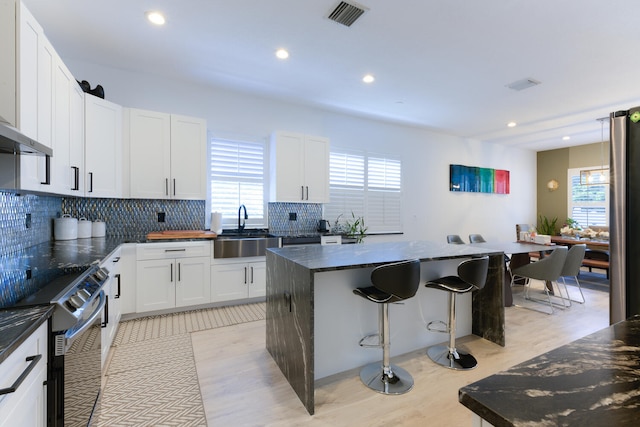 kitchen with visible vents, a kitchen island, a breakfast bar, stainless steel electric range, and a sink