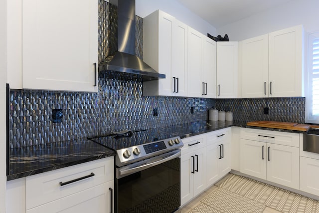 kitchen featuring stainless steel electric range oven, white cabinetry, tasteful backsplash, and wall chimney range hood