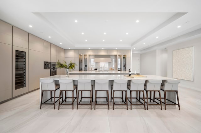 kitchen with a kitchen bar, premium range hood, a raised ceiling, and a large island