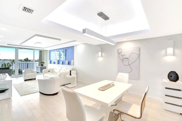 dining area featuring light wood-type flooring, a raised ceiling, and expansive windows