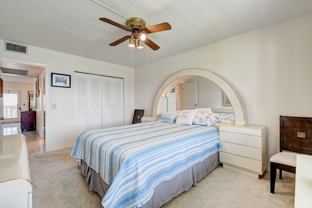 bedroom featuring ceiling fan, light colored carpet, a textured ceiling, and a closet