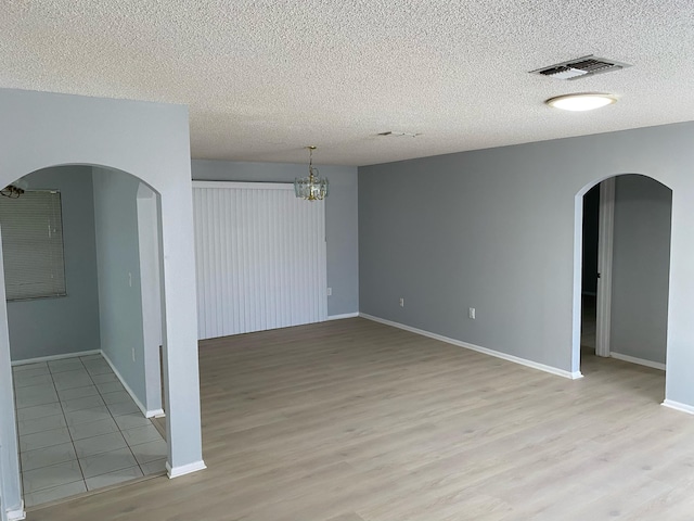 spare room with light wood-type flooring, a textured ceiling, and a chandelier