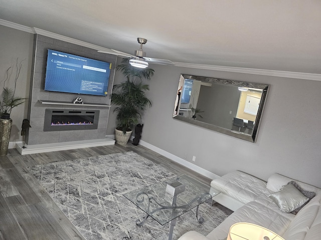 living room featuring ceiling fan, a large fireplace, wood finished floors, baseboards, and crown molding