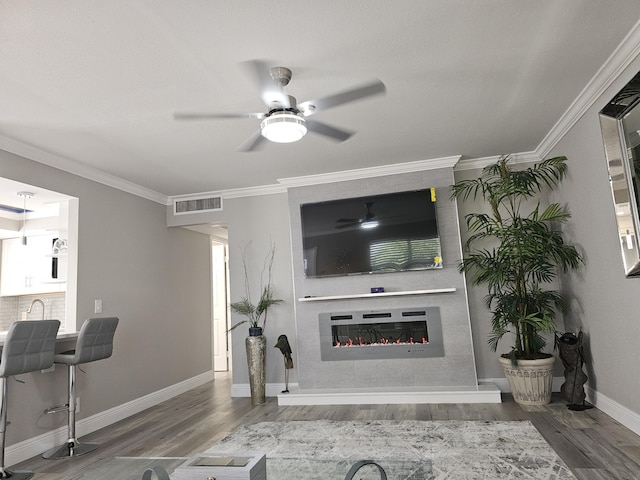 living area with a fireplace, wood finished floors, visible vents, and crown molding