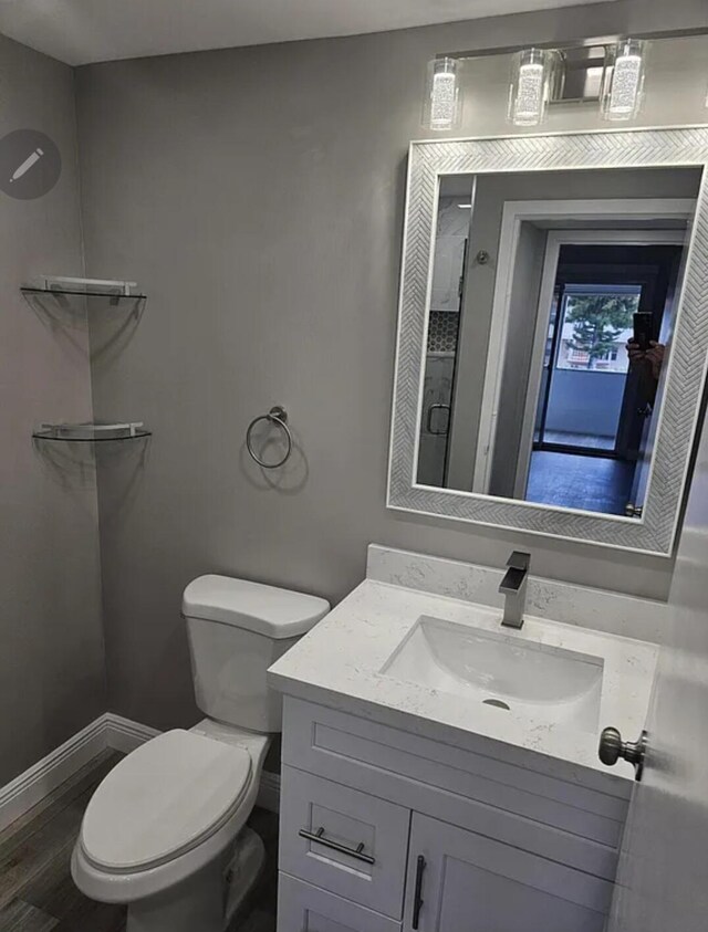 bathroom featuring baseboards, toilet, wood finished floors, walk in shower, and vanity