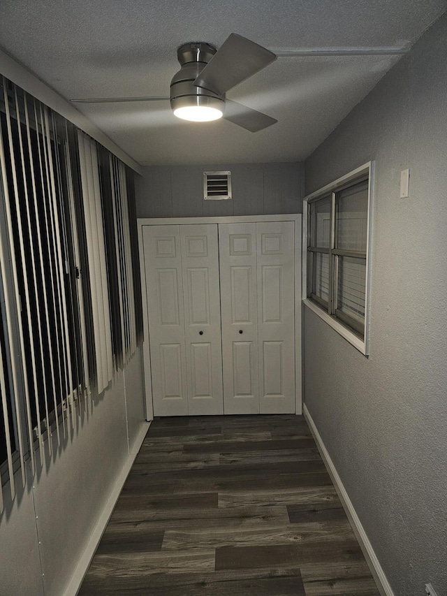 corridor with a textured ceiling, dark wood-style flooring, visible vents, and baseboards