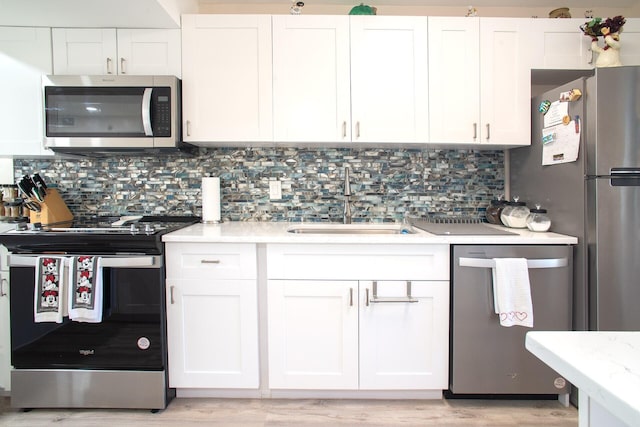 kitchen with appliances with stainless steel finishes, backsplash, white cabinetry, and light hardwood / wood-style flooring