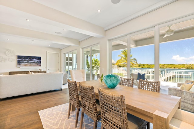 dining area with a water view, beamed ceiling, and hardwood / wood-style flooring