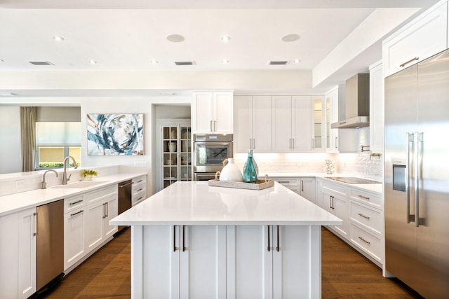 kitchen with dark wood-type flooring, wall chimney range hood, appliances with stainless steel finishes, and a center island