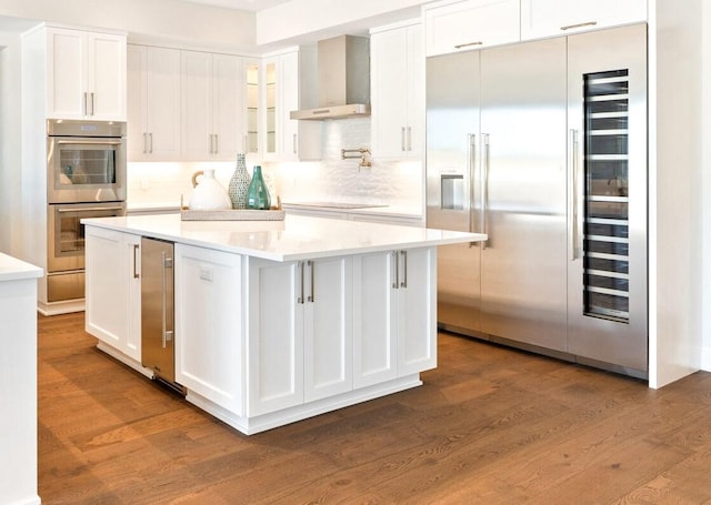 kitchen featuring wall chimney range hood, a kitchen island, stainless steel appliances, and white cabinetry