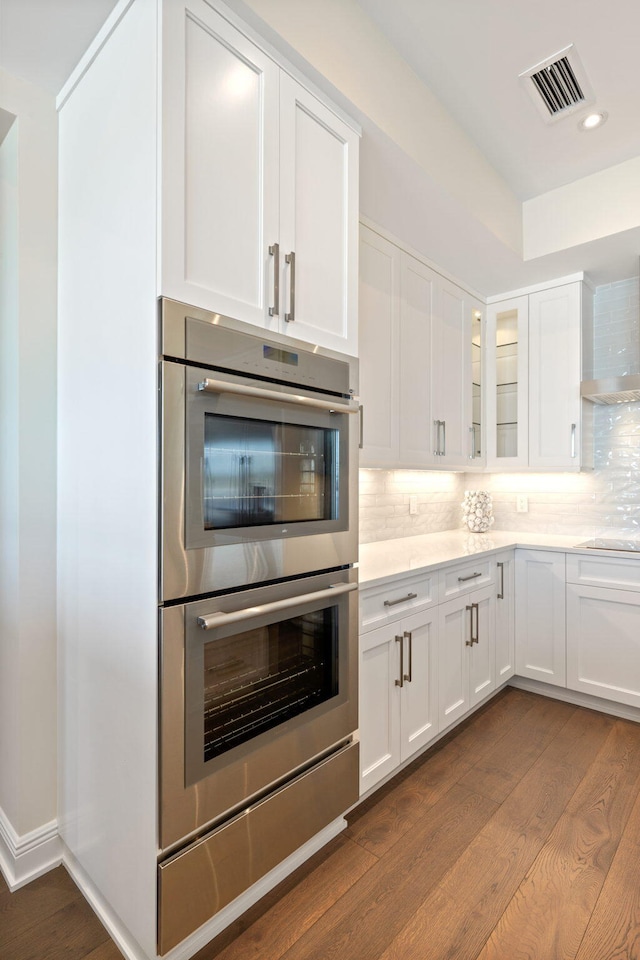 kitchen with stainless steel double oven, backsplash, white cabinets, and dark hardwood / wood-style floors