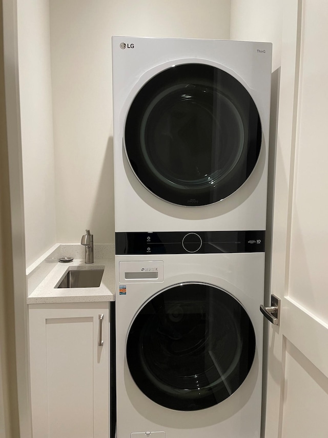 washroom with cabinets, stacked washer and clothes dryer, and sink