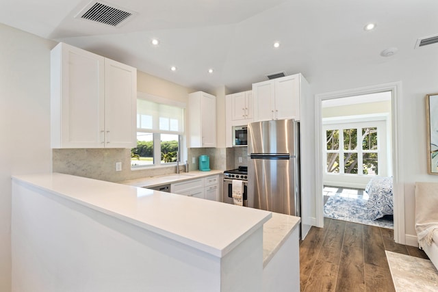 kitchen with dark hardwood / wood-style floors, backsplash, appliances with stainless steel finishes, kitchen peninsula, and white cabinetry