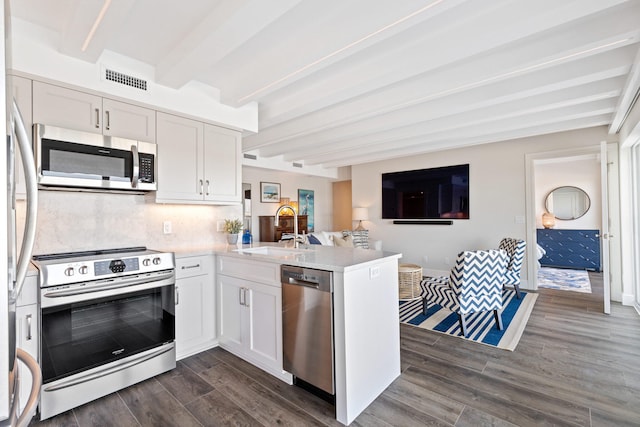 kitchen with appliances with stainless steel finishes, beam ceiling, kitchen peninsula, sink, and white cabinets