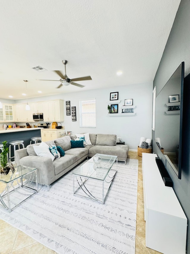 living room with ceiling fan, light tile patterned floors, and a textured ceiling