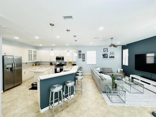 kitchen featuring a kitchen breakfast bar, decorative light fixtures, appliances with stainless steel finishes, a kitchen island with sink, and sink