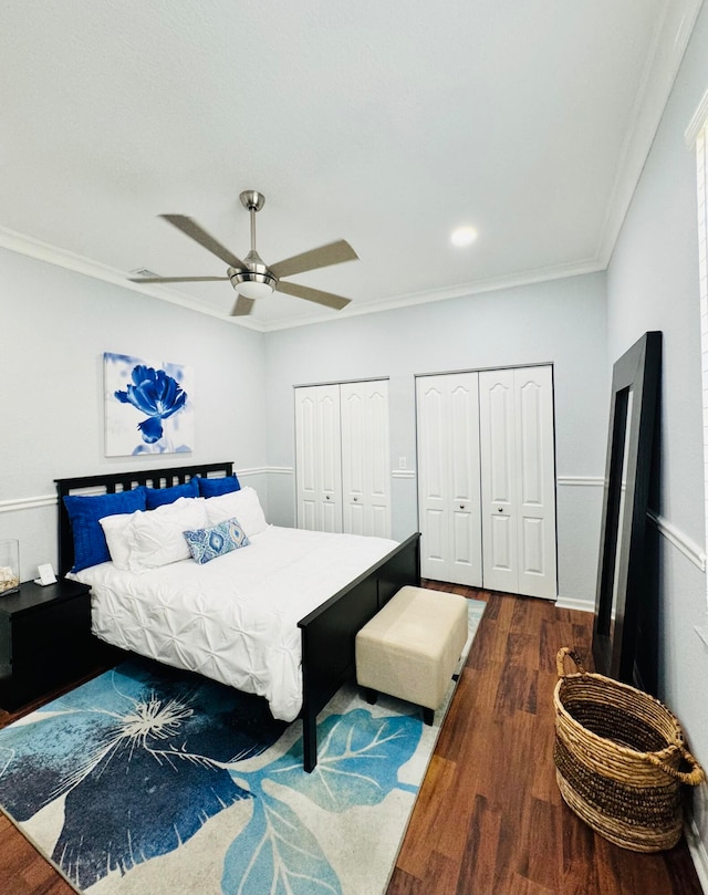 bedroom featuring dark wood-type flooring, ceiling fan, ornamental molding, and two closets