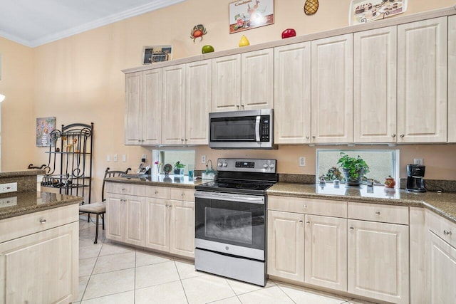 kitchen featuring crown molding, light tile patterned floors, appliances with stainless steel finishes, and dark stone counters