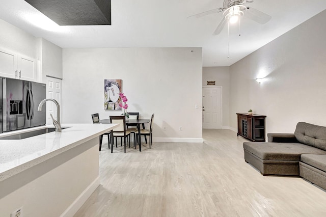 kitchen with sink, stainless steel fridge with ice dispenser, light stone countertops, light hardwood / wood-style floors, and white cabinets