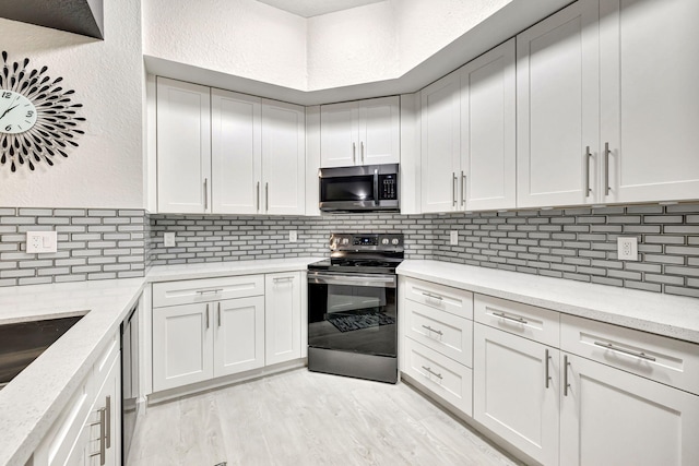 kitchen featuring white cabinetry, light stone counters, stainless steel appliances, and light hardwood / wood-style floors