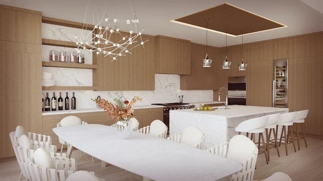 kitchen with light wood-type flooring, tasteful backsplash, stainless steel appliances, a center island with sink, and hanging light fixtures