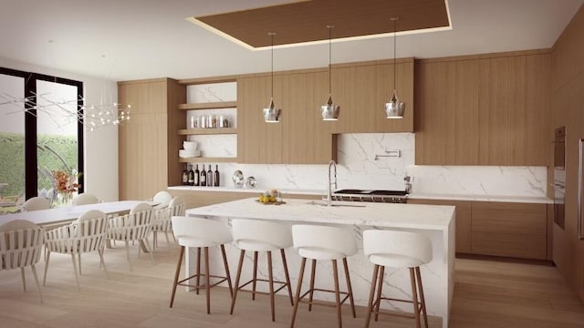 kitchen featuring light stone countertops, a kitchen breakfast bar, light hardwood / wood-style flooring, decorative light fixtures, and a center island with sink