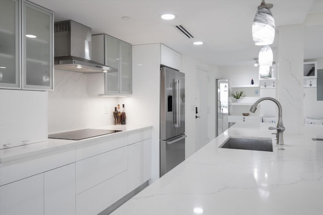 kitchen featuring sink, light stone counters, wall chimney exhaust hood, decorative light fixtures, and high end fridge