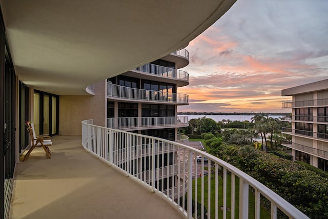 balcony at dusk featuring a water view