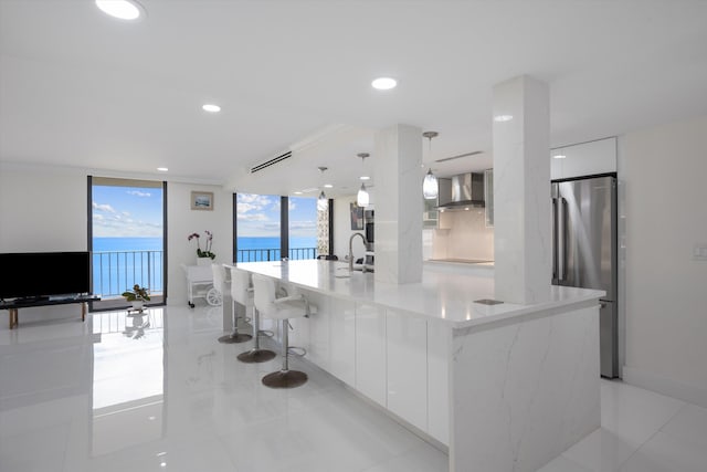 kitchen with a large island, stainless steel refrigerator, pendant lighting, white cabinets, and wall chimney exhaust hood