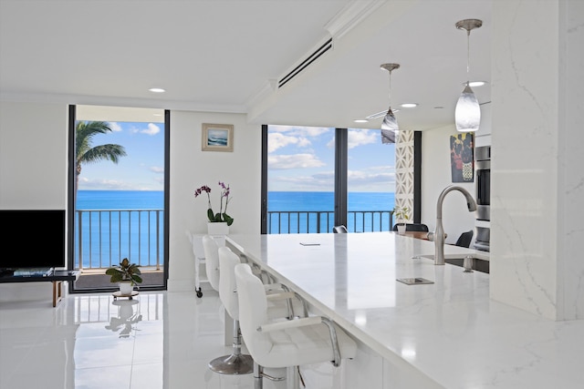 kitchen featuring sink, a water view, light stone counters, light tile patterned floors, and pendant lighting