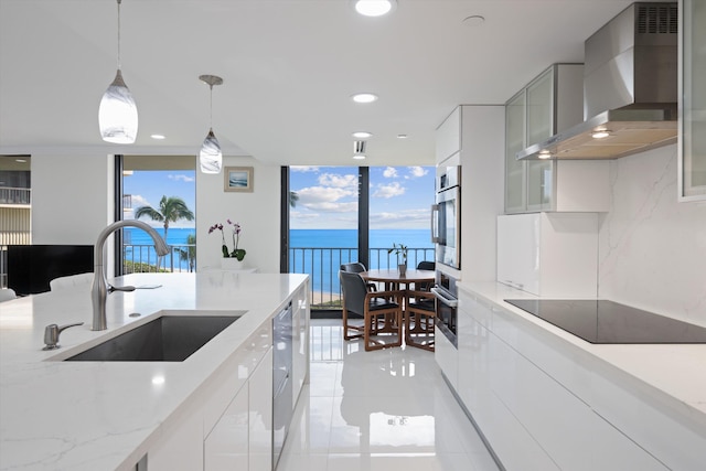 kitchen featuring appliances with stainless steel finishes, sink, white cabinets, a water view, and wall chimney exhaust hood