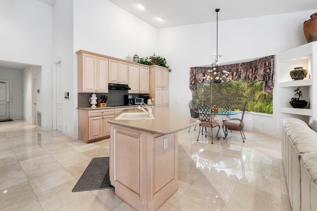 kitchen featuring light brown cabinetry, sink, pendant lighting, a kitchen island with sink, and a towering ceiling