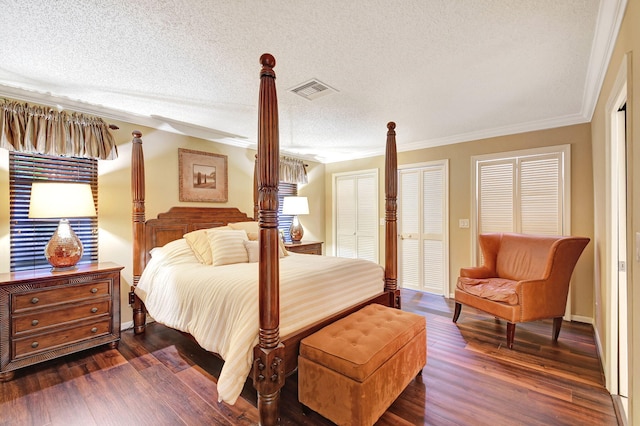 bedroom featuring a textured ceiling, dark wood-type flooring, ornamental molding, and multiple closets