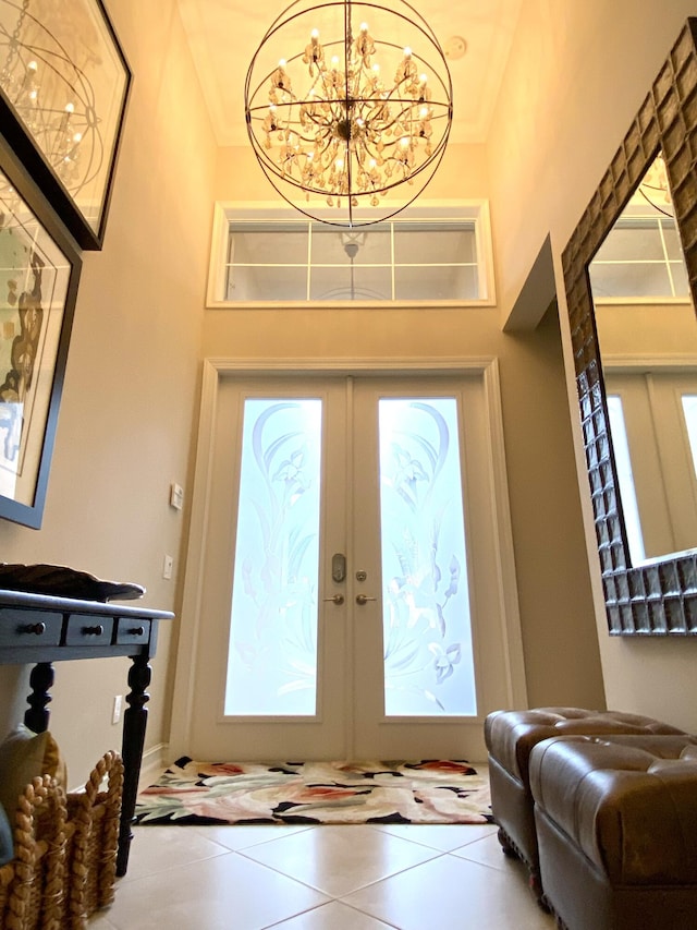 tiled entrance foyer featuring crown molding, a high ceiling, an inviting chandelier, and french doors