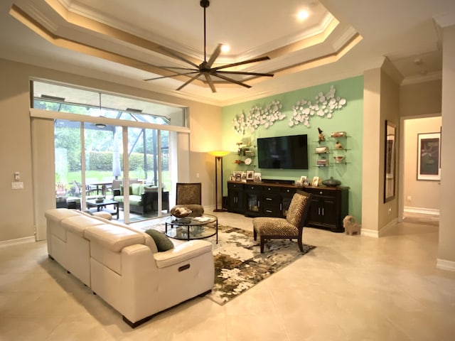 living room with a tray ceiling, ceiling fan, crown molding, and light tile patterned flooring