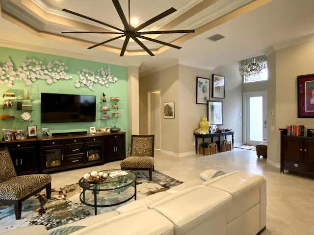 living room with light tile patterned floors, crown molding, ceiling fan with notable chandelier, and a tray ceiling