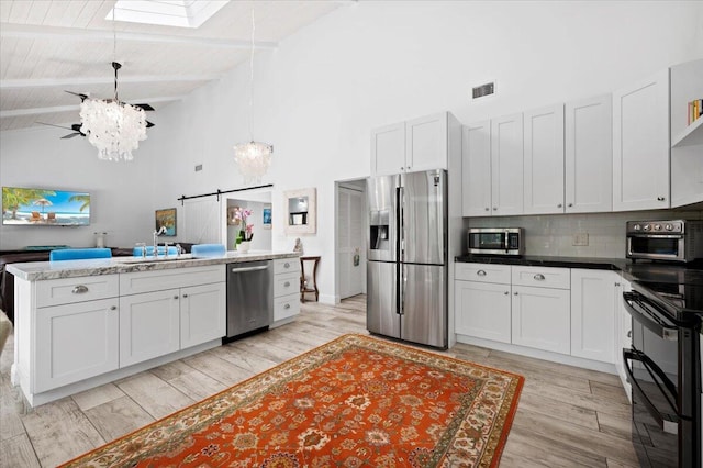 kitchen with a skylight, a barn door, light wood-type flooring, stainless steel appliances, and beam ceiling