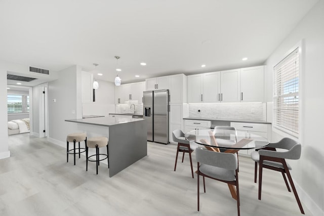 kitchen with a healthy amount of sunlight, backsplash, white cabinets, and stainless steel refrigerator with ice dispenser