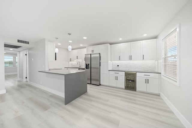 kitchen with stainless steel fridge with ice dispenser, a wealth of natural light, kitchen peninsula, and hanging light fixtures