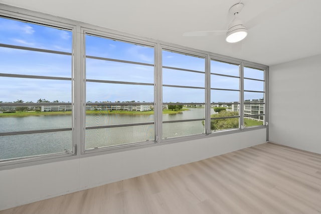 unfurnished sunroom featuring ceiling fan and a water view