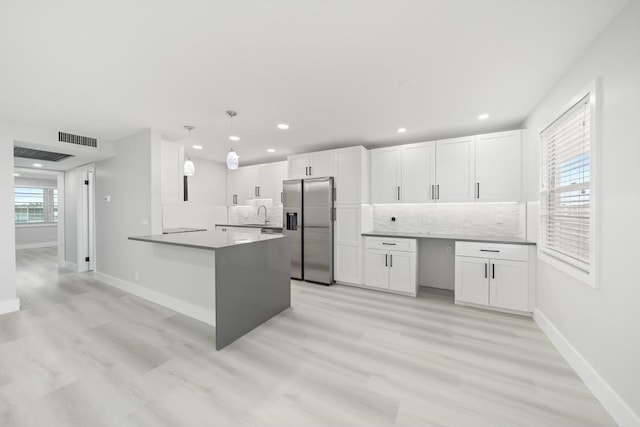 kitchen with stainless steel fridge with ice dispenser, a healthy amount of sunlight, kitchen peninsula, and decorative light fixtures