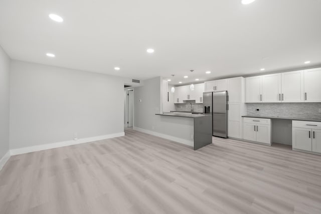 kitchen with stainless steel fridge, decorative backsplash, white cabinetry, and light hardwood / wood-style floors