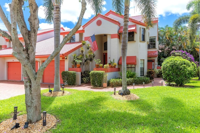 mediterranean / spanish house with driveway, stucco siding, a front lawn, a garage, and a tile roof