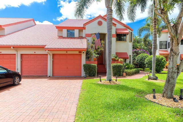 mediterranean / spanish house with stucco siding, a tile roof, decorative driveway, a front yard, and a garage