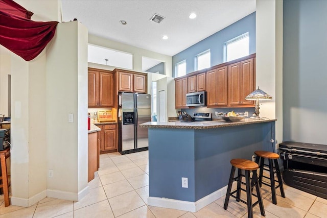 kitchen featuring appliances with stainless steel finishes, kitchen peninsula, light tile patterned flooring, a breakfast bar area, and a textured ceiling